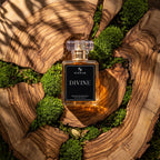 A glass perfume bottle labeled 'SIGBAR DIVINE' sits centered on a polished wood slice surrounded by green moss. The bottle has a clear cap and a black front label with white text.