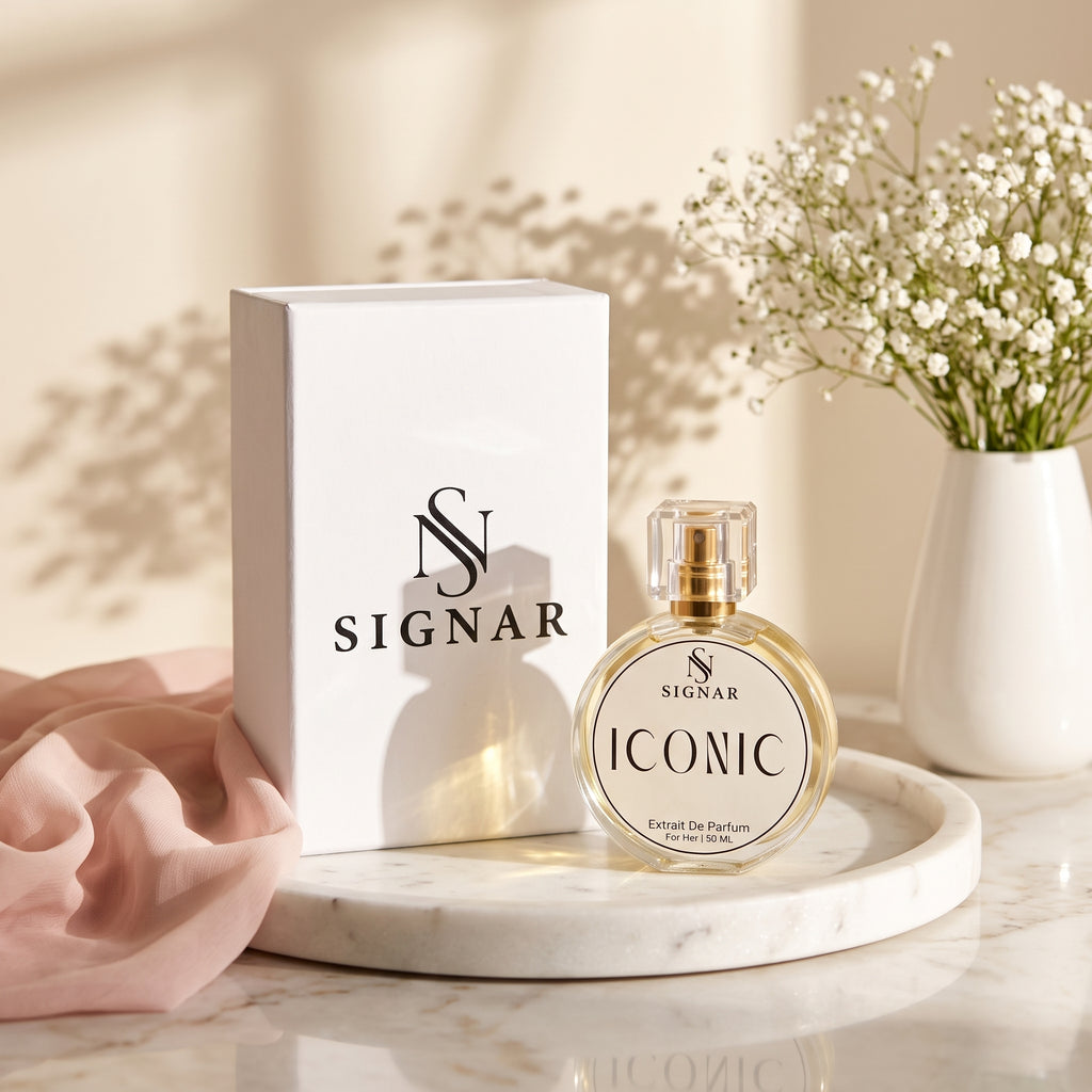 SIGNAR Iconic Extrait de Parfum perfume bottle displayed next to its white packaging box on a marble tray, with a pink fabric accent and a vase of baby's breath in the background.