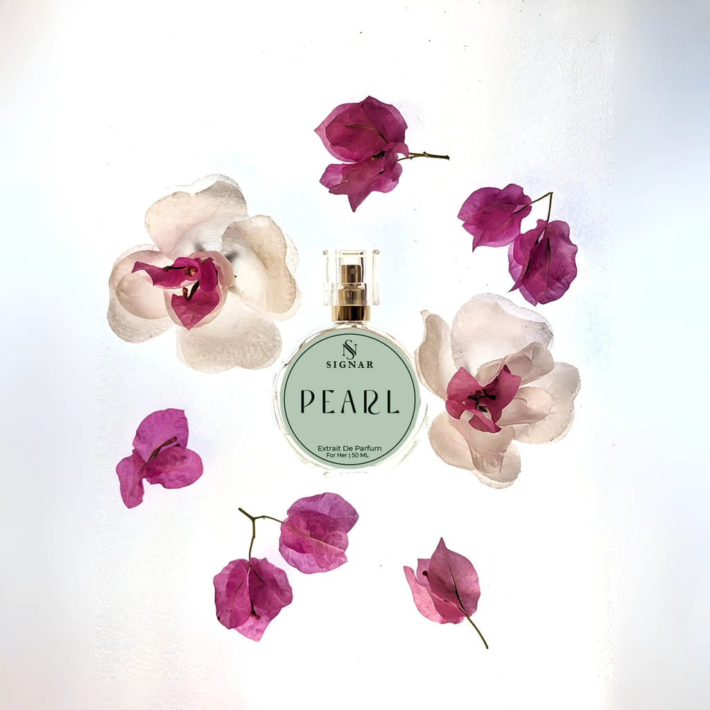 A round glass perfume bottle labeled 'SIGNAR PEARL' with a gold cap, arranged on a white background with decorative pink and white flowers around it.