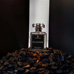 A glass perfume bottle labeled 'SIGNAR PHANTOM' stands centered on a bed of dark pebbles, with a tall white illuminated backdrop behind it.