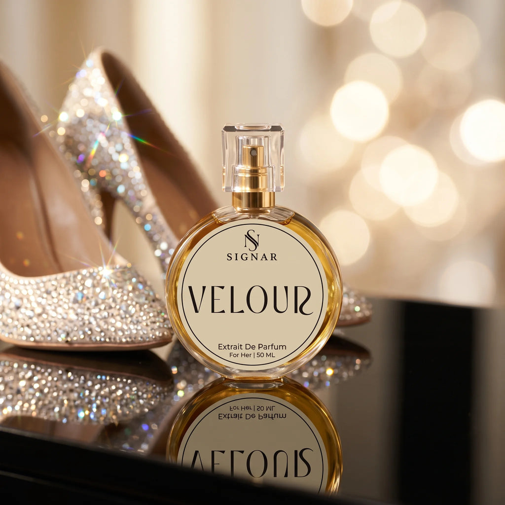 SIGNAR VELOUR Extrait De Parfum for her in a round gold-toned bottle, styled next to sparkling silver high-heeled shoes on a reflective black surface with a warm bokeh background.