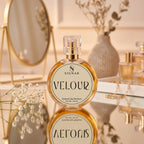 SIGNAR VELOUR Extrait De Parfum for her, 50 mL, in a round clear glass bottle with a gold spray pump and cream-colored label, displayed on a reflective surface with a gold mirror and dried flowers in the background.