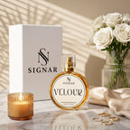 SIGNAR VELOUR extrait de parfum bottle with its white packaging box, styled on a marble surface with a candle, white roses, and gold rings under soft window shadows.
